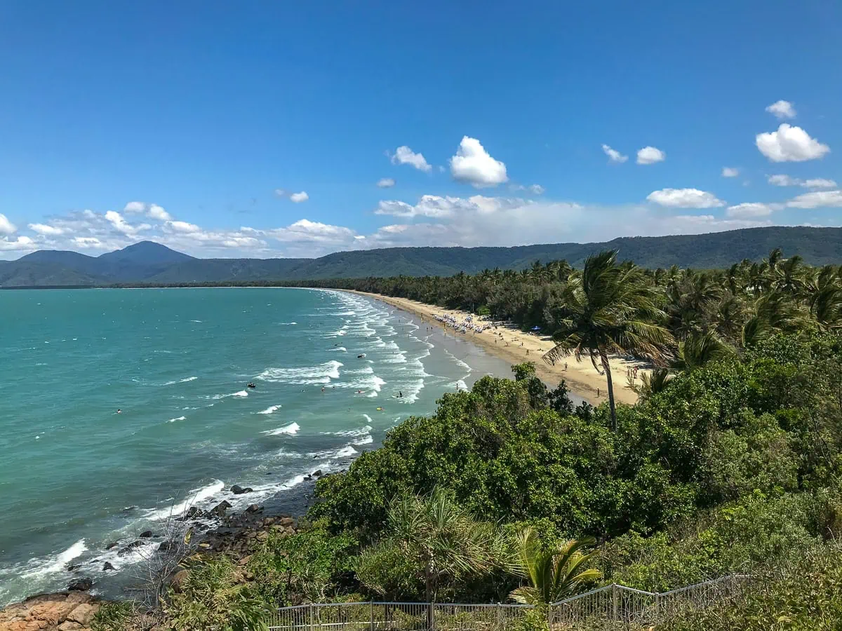 green trees and light blue coloured ocean water with white waves breaking into the sandy beach